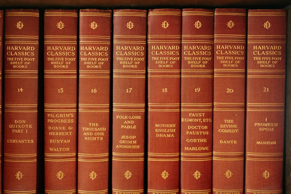 A row of classic literature volumes from the Harvard Classics series on a wooden shelf.