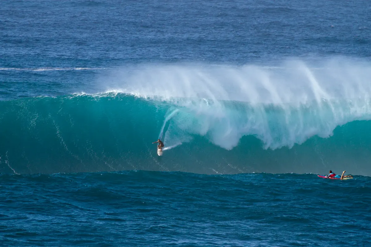 Surfer riding massive wave in Hawaii with vibrant blue ocean and dramatic surfing scene.