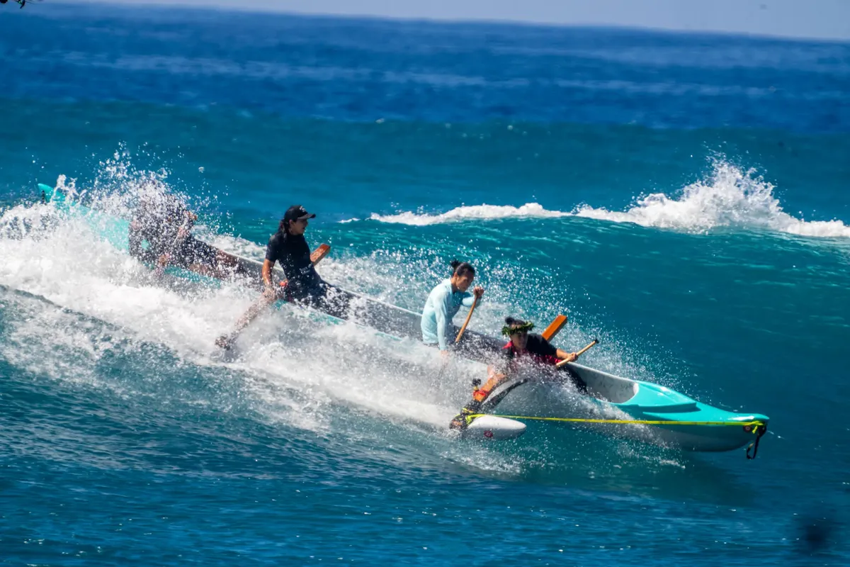 A vibrant scene of people paddling an outrigger canoe through waves in Hawaii.